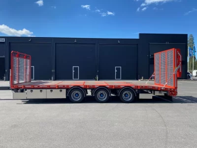 Röd maskintransport framför större svart byggnad.