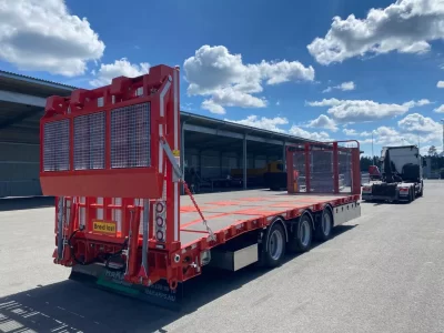 Röd maskintransport med lastbild i bakgrunden.