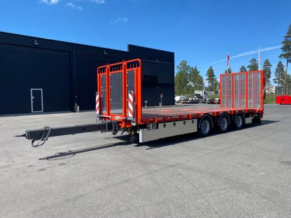 Röd maskintransport med träd, flaggor och byggnader i bakgrunden.
