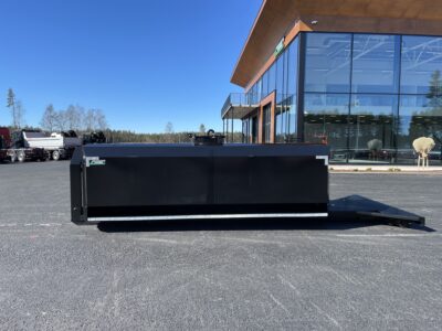 Vattentank i svart på lastväxlarram från sidan framför byggnad.