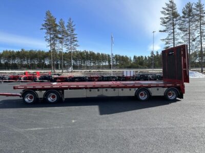 Röd maskinvagn med uppfälld ramp med träd och väg i bakgrunden.