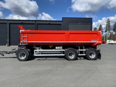 En röd dumpervagn sedd från sidan med ett större garage i bakgrunden.