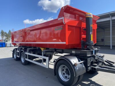 En röd dumpervagn framför plåtbyggnad.