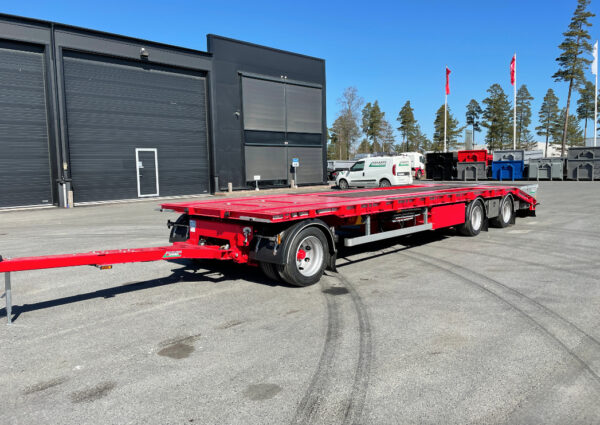 Röd kombivagn framför flaggor och träd på gårdsplan.