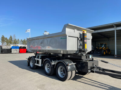 Grå dumpervagn med gul traktor i bakgrunden.