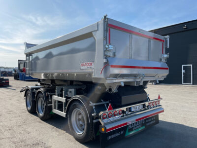 En grå dumperkärra framför svart garage.