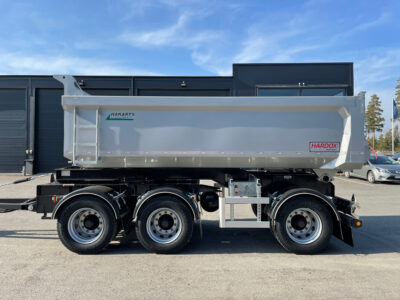 Grå dumpervagn framför svart byggnad.