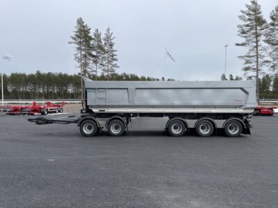 Grå dumpervagn med låsbar vändkrans från sidan med träd och flagga bakom.