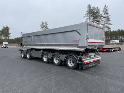 Grå dumpervagn med låsbar vändkrans snett bakifrån med träd i bakgrunden.