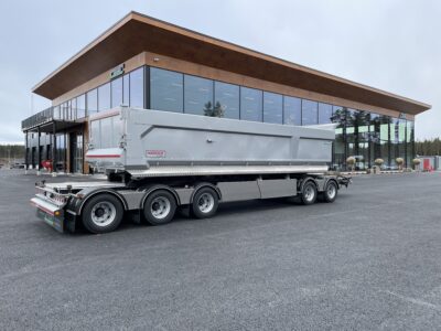 Grå dumpervagn med låsbar vändkrans snett bakifrån med byggnad i bakgrunden