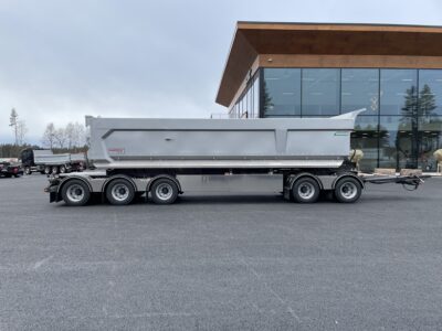 Grå dumpervagn med låsbar vändkrans från sidan med byggnad bakom.