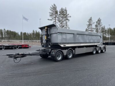 Grå dumpervagn med låsbar vändkrans snett framifrån med flera träd bakom.