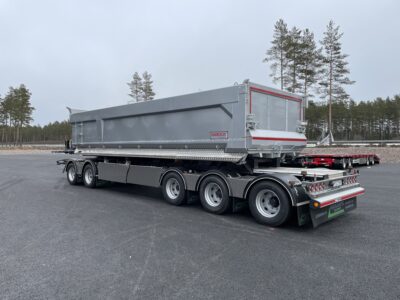 Grå dumpervagn med låsbar vändkrans snett bakifrån med träd bakom.