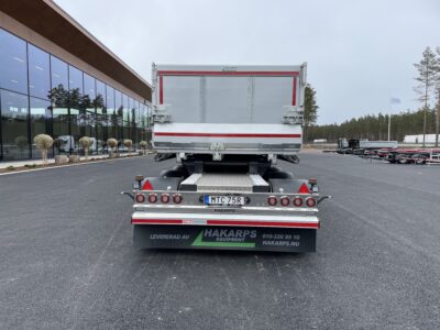 Grå dumpervagn med låsbar vändkrans bakparti med lastväxlarvagnar och byggnad i bakgrunden.