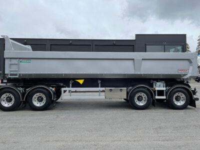 Grå dumpervagn framför stor byggnad.