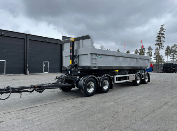 Grå dumpervagn med träd och flaggor bakom.