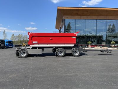 röd 30 ton dumperkärra från sidan framför byggnad.